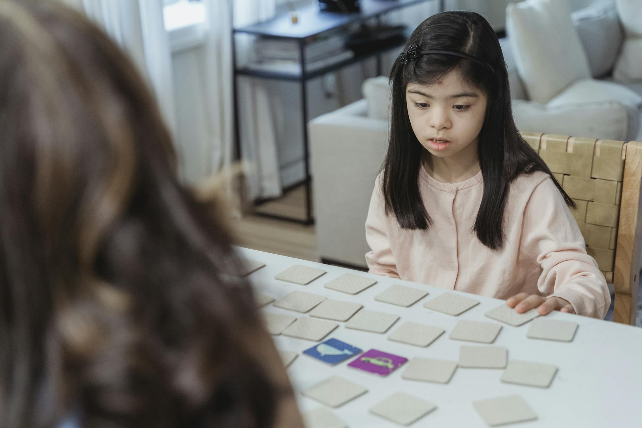 Young girl with Down syndrome focuses on a memory game at a home table.